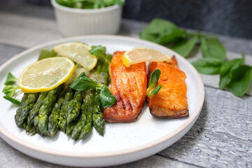 Baked salmon and asparagus with salad and lemon on dark background. Top view. 