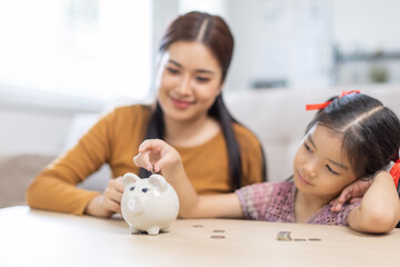 Setting good example. Young parent mother teach child little daughter girl to manage finances save money spend earnings with economy plan family budget. Friendly mom and kid thrift coins in piggybank
