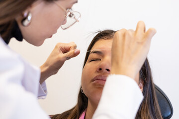 Beautician doing eyebrow threading design procedure. Young latin woman in a professional beauty salon for threading and brow shape correction