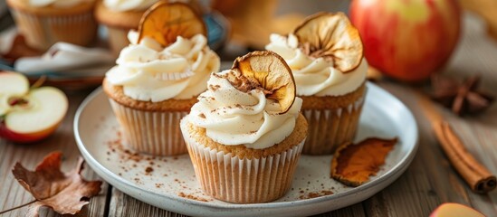 Autumn-themed apple cupcakes topped with cream cheese frosting, dried apple slices, and cinnamon, placed on a ceramic plate with a close-up view. Ideal for a fall dessert with copy space.