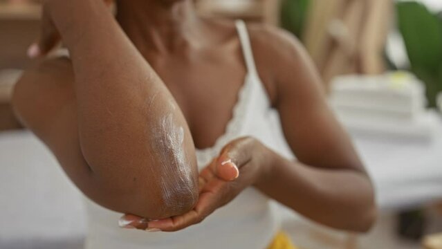 African american woman applying lotion to her elbow in a spa, highlighting her wellness routine in an indoor salon setting.