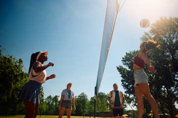 Below view of young people playing volleyball on the beach.