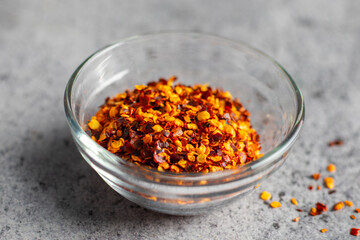 Aromatic food appetizer red chilli flakes in glass jar with ceramic background. Selective focus.  