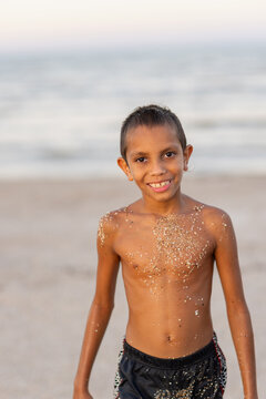 aboriginal boy on beach with sand stuck to him from where he has been playing