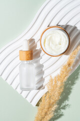 Moisturizer open cream jar, serum in glass bottle on white podium with pampas reeds with copy space. Set for skin and body care beauty products. unbranded package, showcase