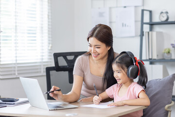 Asian business lady working on computer while her daughter hugging her