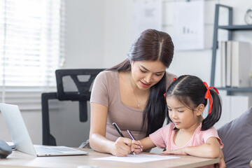 Asian business lady working on computer while her daughter hugging her