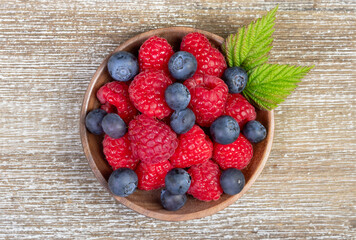 Plate with raspberries and blueberries with leaves on the wooden rustic table.