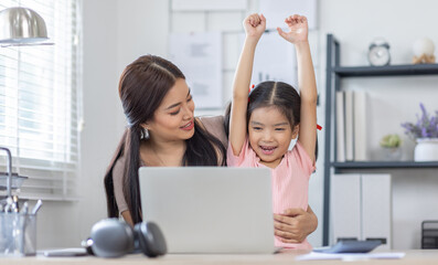 Asian business lady working on computer while her daughter hugging her