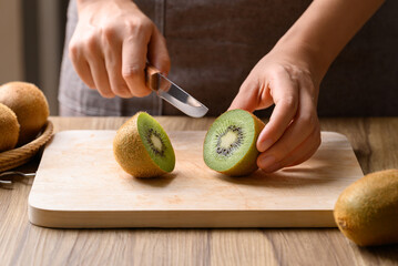 Hand holding kitchen knife and cutting kiwi fruit on wooden board, Homemade cooking