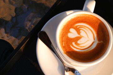 Hot coffee with heart latte art on top for welcoming a new morning. Close-up latte art coffee in a white cup with natural light. Concept of caffeine, heart, energy drink, enjoying a cup of hot latte.