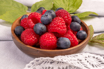 Plate with raspberries and blueberries on the wooden table with laced cloth.
