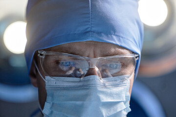 Extreme closeup of focused male surgeon wearing protective glasses and mask performing surgery in...