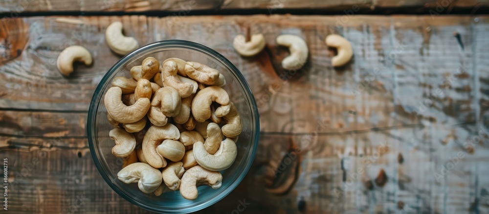 Poster Top view of a glass bowl filled with raw cashew nuts displayed on a wooden table, creating a serene copy space image.