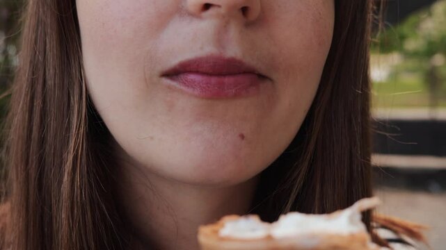 Closeup of young unrecognizable unknown woman biting cold ice cream while sitting on a bench on a city street enjoying frozen dessert having snack on summer day