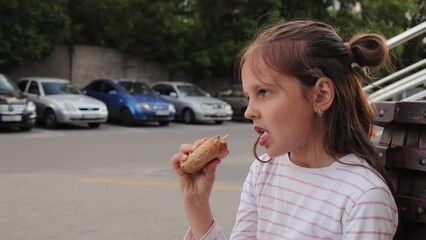 Adorable brown haired little girl with hair bun eating ice cream outdoors in summer when it's hot outside female child resting on summer holidays sitting on bench