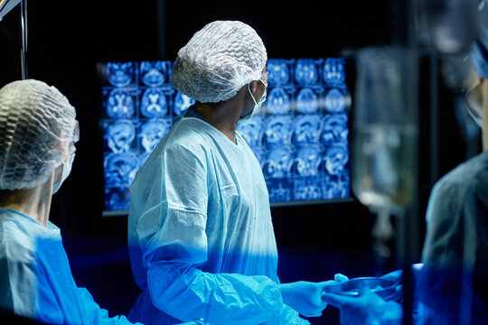 Waist up portrait of female surgeon performing brain surgery in operating room and looking at monitor with scans copy space