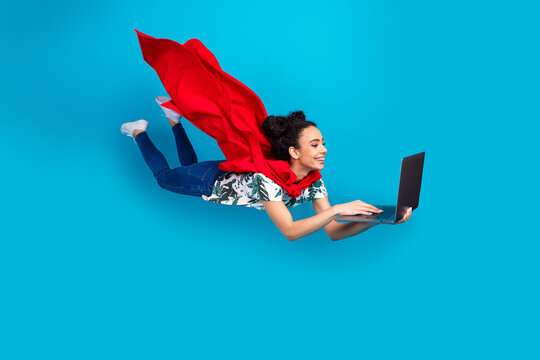 Full size photo of nice young girl superhero costume fly use laptop isolated on blue color background