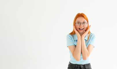 Photo of anxious stressed woman looks with frightened expression keeps hands under chin reacts on something horrible wears blue t-shirt against white wall.