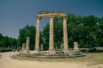 Fototapeta premium View of archeological ruins consisting of different columns or pillars taken on a sunny day in the ancient site of Olympia, Greece