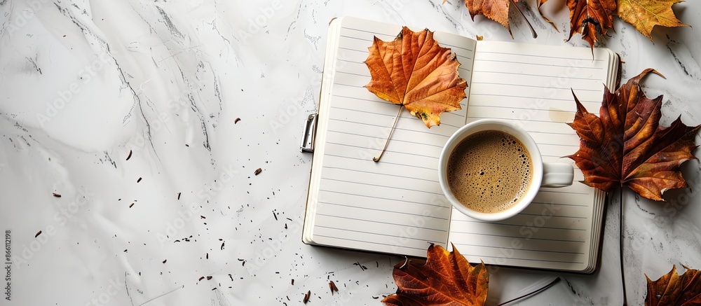 Poster autumn leaves and a coffee cup on a white grunge backdrop in a blank notebook with copy space image.