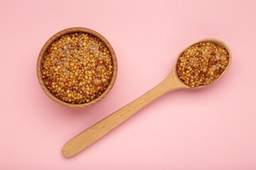French grain mustard in bowl and spoon on pink background.