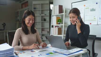 Two confident businesswomen using laptops in the office Happy female entrepreneurs smile while working together in modern workspace. Concept of teamwork, meeting, brainstorming.