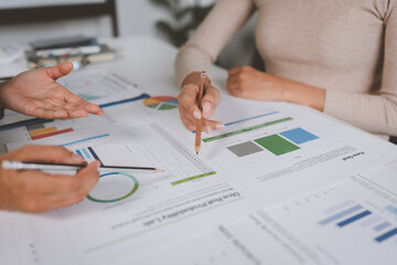 Two businesswomen meet, discuss, brainstorm, point at graphs and charts to analyze online market data, calculate balance sheets, accounts, net profit to plan company sales strategies.