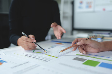 Two businesswomen meet, discuss, brainstorm, point at graphs and charts to analyze online market data, calculate balance sheets, accounts, net profit to plan company sales strategies.