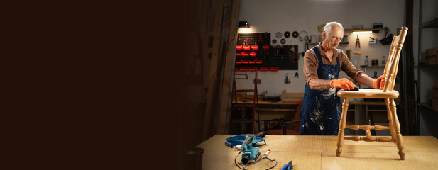 Fototapeta premium furniture repair, DIY and home improvement concept. elderly man in orange gloves sanding wooden chair with sandpaper, preparing surface for further processing.