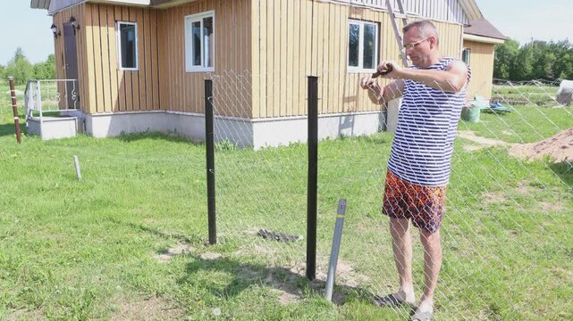Chain-link fence is built on garden plot in nature, landowner twists ends wire of chainlink fence together.