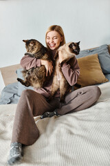 Obraz premium A serene woman with short hair sits on a bed, holding two cats close to her, enjoying a peaceful moment at home.