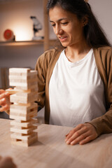 Woman smiling while playing wooden block game at home, engaging in leisure activity