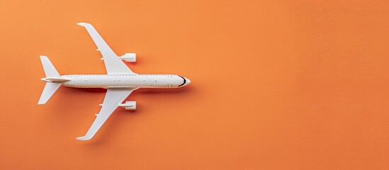 A white airplane model placed on an orange background symbolizes vacation travel on a summer-themed flat lay image with a top view and ample copy space.