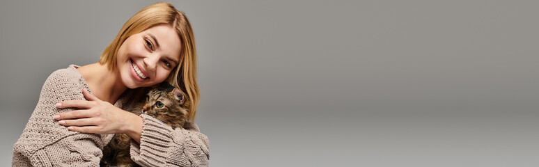 A woman with short hair smiles, holding her arm around her neck in a joyful embrace, sharing a moment of connection with her cat.