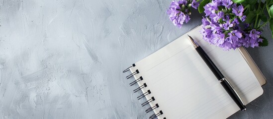 Naklejka premium Flat lay with a notebook, a pen, and a purple flower arranged on a gray backdrop, seen from a top view, creating a composition with copy space image.