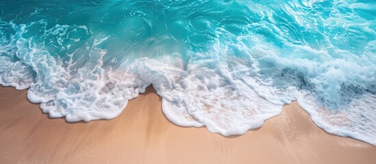 Fototapeta premium Turquoise ocean waves gently caressing a sandy beach, captured in a high-angle copy space image.