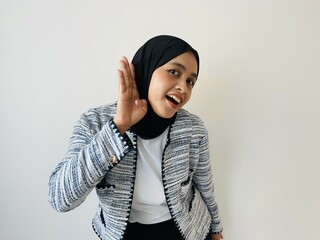 Amazed beautiful Muslim Asian woman puts a hand to the ear to hear better. Young woman listening something over white background. Deafness concept. Woman holds her hand near ear and listens carefully