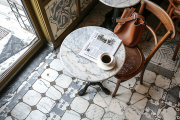Top view of an empty table in a vintage Parisian cafe. On the table are a cup of coffee and a newspaper