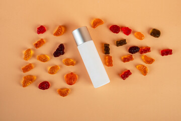 Cosmetic product in tube, bottle, lotion or serum and colorful candies, jelly on cream background. 