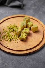 Traditional Middle Eastern confectionery, pistachio flavored Turkish delight (lokum) cut into cubes and displayed on a round wooden serving board.