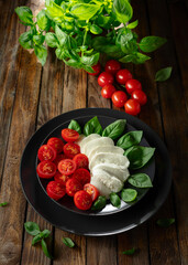 Mozzarella with basil and cherry tomatoes on an old wooden table.