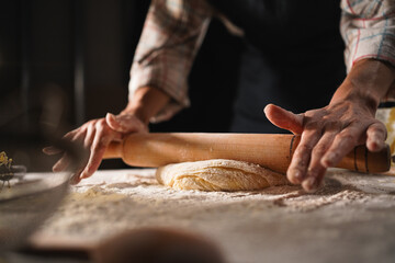 Close-up of hands rolling out a wooden rolling pin dough for pizza on the table