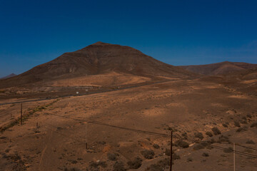 Rugged Beauty: A winding dirt path meets a modern highway in the desert landscape of Fuerteventura. Islands iconic volcanic formation stands sentinel over the barren yet captivating scenery.