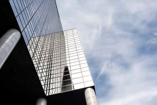 Modern architecture showcasing a reflective glass building facade under a slightly cloudy sky, highlighting the sleek design elements and urban aesthetic of contemporary structures.