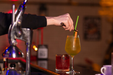Close-up of a bartender decorating a cocktail with a cinnamon stick and a straw on the bar counter. Concept of making cocktails