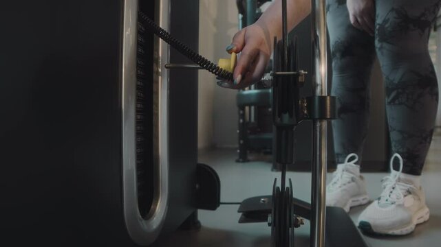 Cropped shot of unrecognizable plus size woman adding weight bars on gym machine during workout