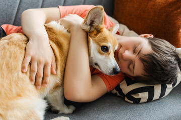 Boy, teenager with down syndrome relaxing on sofa at home embracing corgi dog © Maria Vitkovska