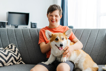 Happy teenager with down syndrome relaxing on sofa at home hugging corgi dog looking at camera © Maria Vitkovska