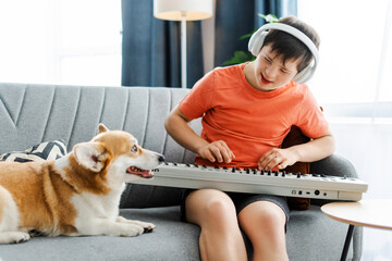 Young boy, teenager with down syndrome playing music on keyboard synthesizer with dog